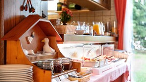 A breakfast buffet with a wooden duck house, plates, and various food items. - Hotel Garni Silberdistel (Hinterzarten)