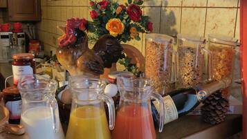 Uma bancada de cozinha com diversos objetos, incluindo uma figurineha de galo, arranjos de flores e recipientes com comida e bebidas.