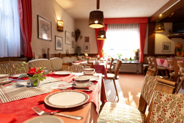 A dining area with a long table set for a meal, surrounded by chairs with floral upholstery.