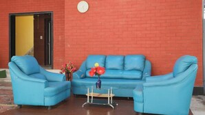 A room with a blue sofa set, a small table with a vase of flowers, and a clock on the wall. - Green Tree Hotel (Chennai)