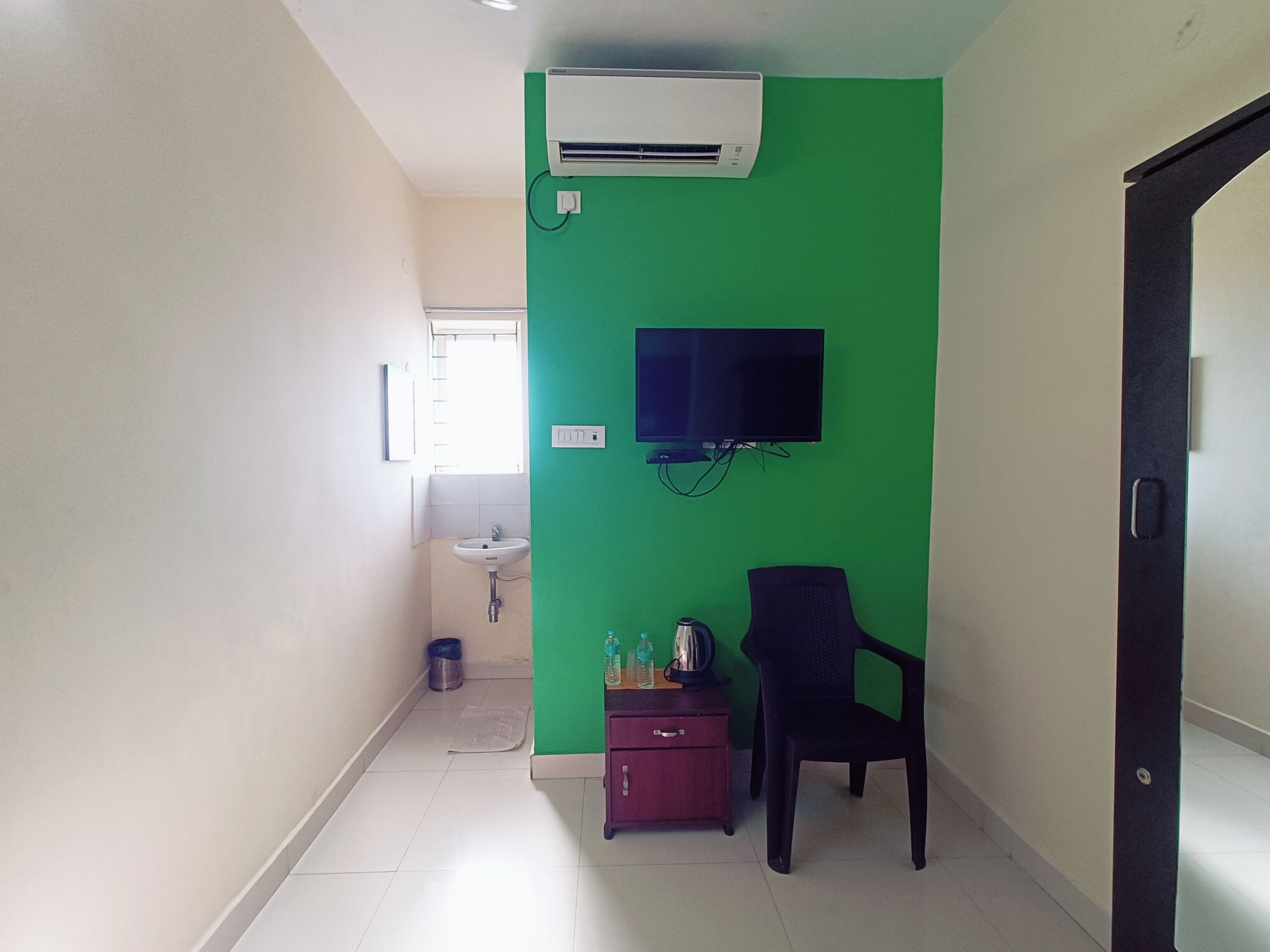 A hallway with a green wall, a mounted TV, a small cabinet, and a chair.