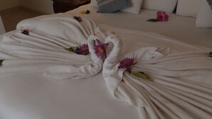 Una cama bien hecha con toallas dispuestas en forma de cisne, decorada con flores moradas.