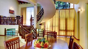 Un comedor con una mesa de madera, sillas y una cesta de frutas. Una escalera con barandilla de madera conduce a otro nivel.