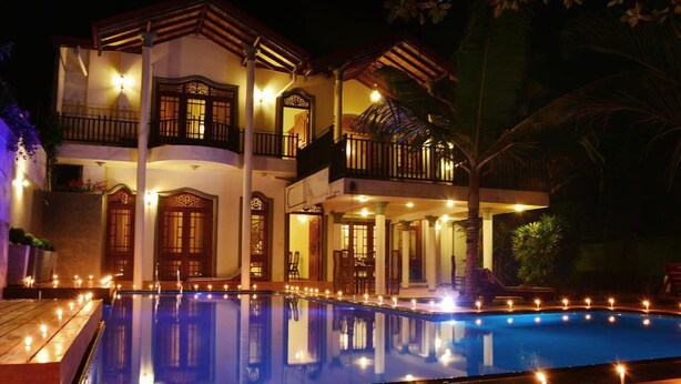 Un edificio de dos pisos con piscina, varios balcones e iluminación exterior.