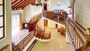 Un interior espacioso con una escalera de madera que conecta dos plantas, un comedor con mesa redonda y un balcón con vistas.