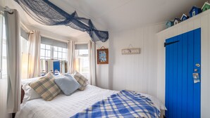 A bedroom with a bed, a blue door, a window, and a wall-mounted shelf with items.