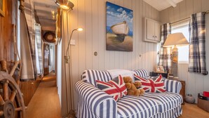 A room with a striped sofa, a lamp, a painting of a boat, and a wooden wheel.