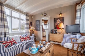 A cozy living room with a sofa, a coffee table with tea set, a television, and a painting on the wall. - A converted boat which overlooks Snettisham RSPB reserve (King's Lynn)