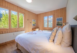 A wooden-paneled room with a bed, two windows, a poster, and a radiator. - Chalet Sonneck - stylish apartment with garden (Wengen)