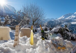 A snowy outdoor setting with a bottle of champagne, glasses, and a snow-covered tree. - Chalet Sonneck - stylish apartment with garden (Wengen)