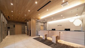 Zona de recepción moderna de hotel con techo de madera, mostrador de recepción y área de espera con bancos.