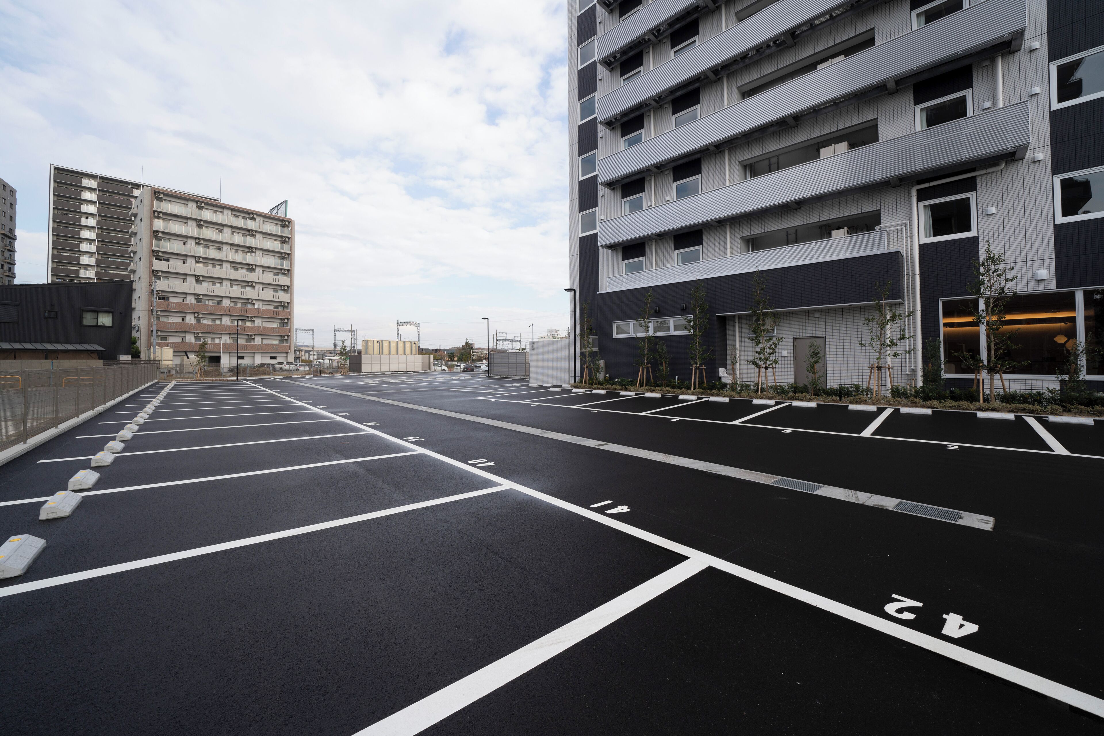 A parking lot with marked spaces and a modern building with multiple floors and balconies.