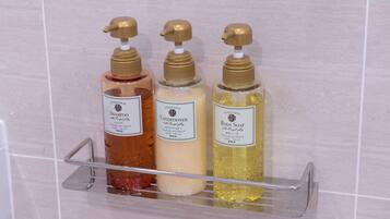 Three bottles of shower products on a metal rack against a tiled wall.