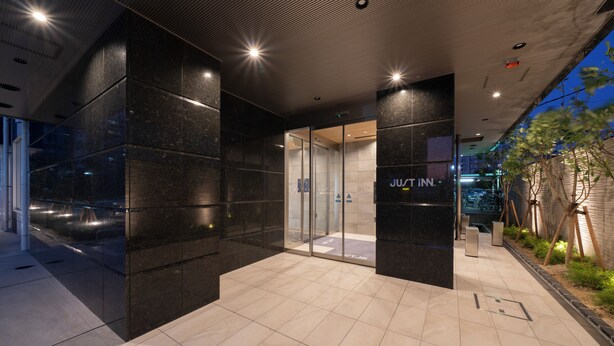 Una entrada de hotel moderna con puertas de cristal, piso de baldosas y un letrero que dice "JUST INN".
