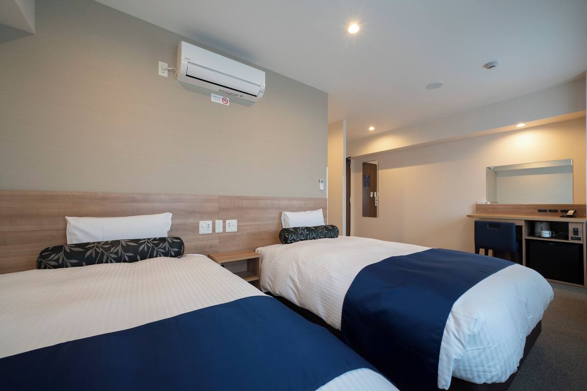 Quarto de hotel com duas camas, uma escrivaninha, um espelho e um ar condicionado.