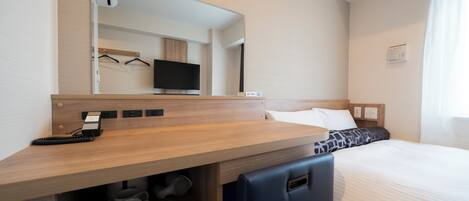 Habitación de hotel con un escritorio de madera, un espejo, una cama con ropa blanca, un televisor pequeño y una cafetera.