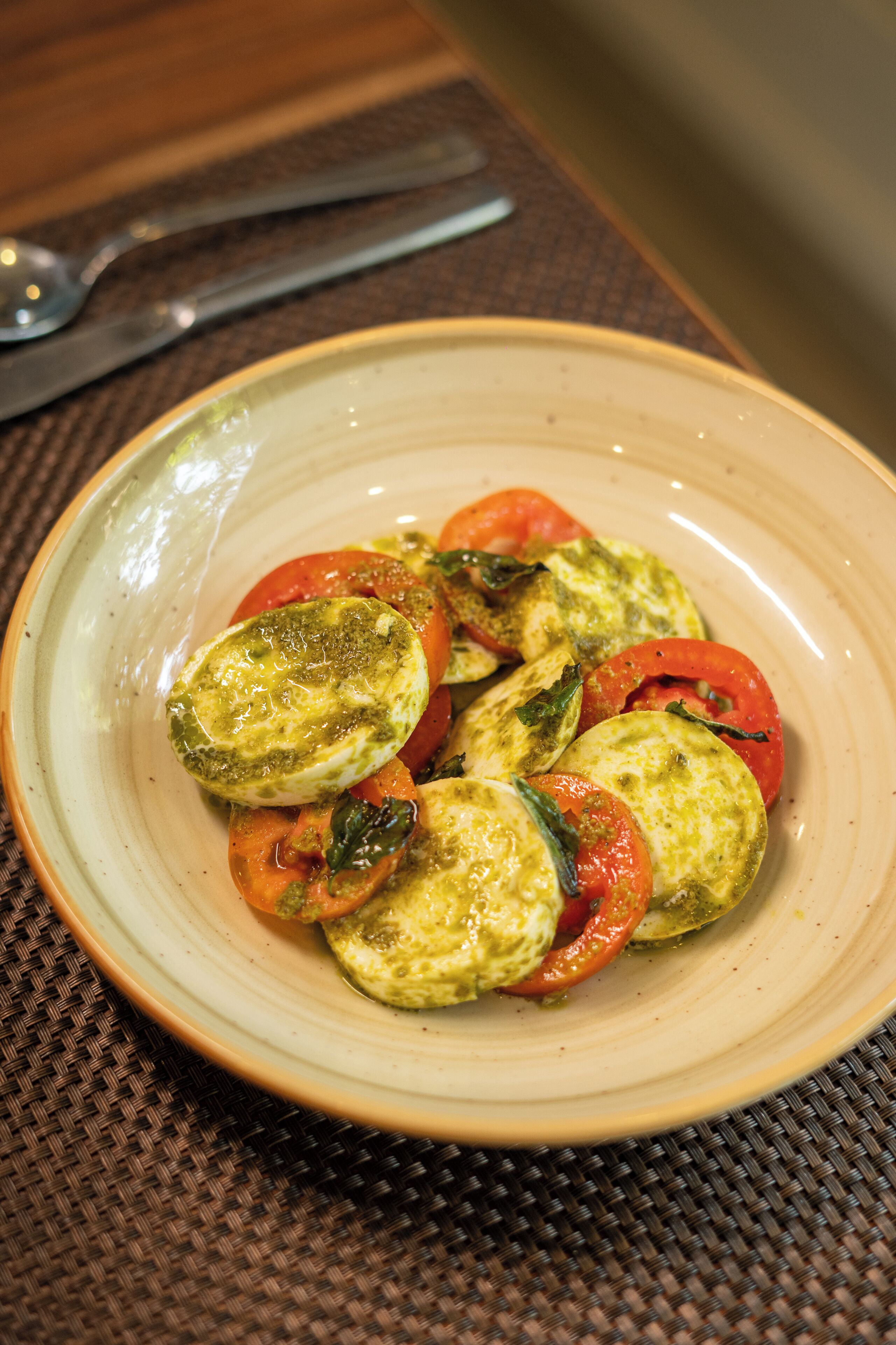 A plate of food with tomatoes and a green sauce, placed on a woven mat.