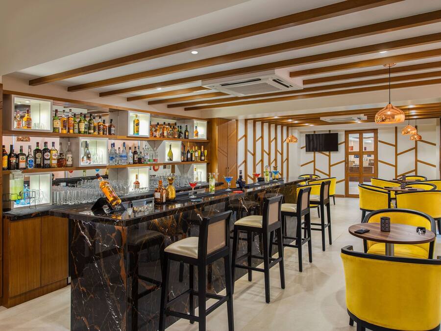 A bar area with a marble counter, multiple liquor bottles, and yellow chairs.