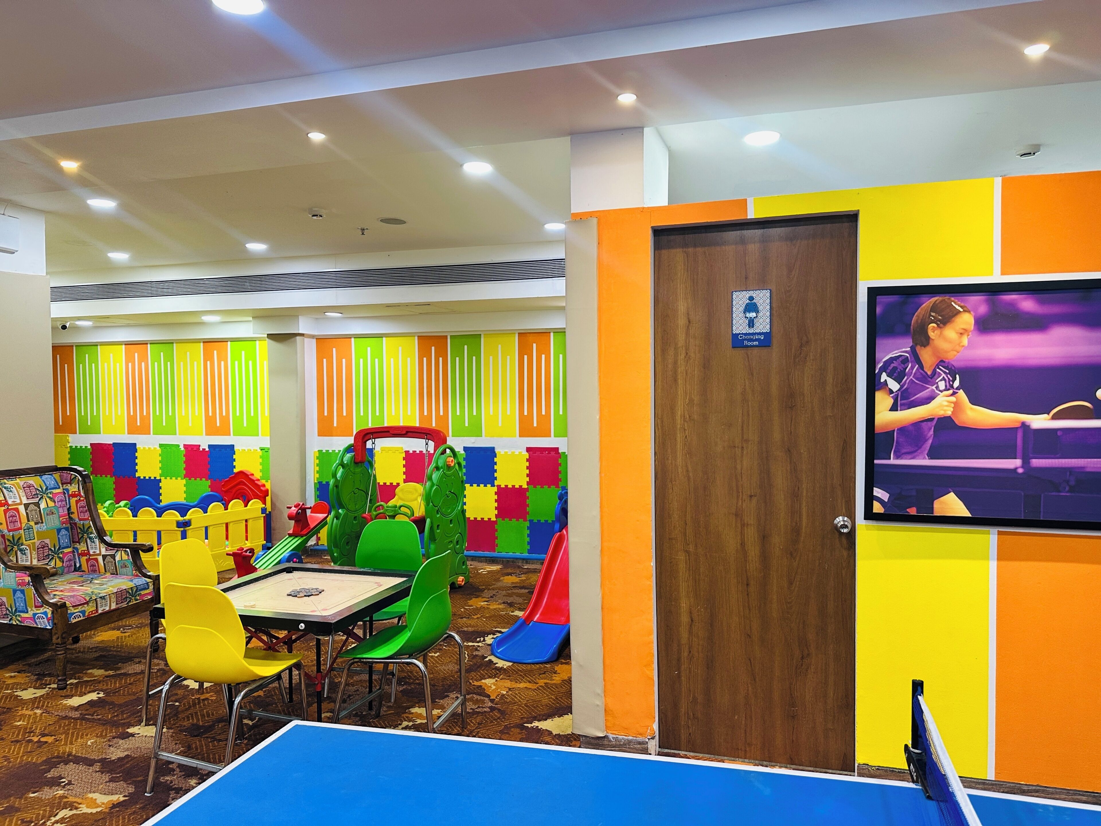 Zona de juegos infantiles con esterillas de espuma de colores, un tobogán y una mesa de ping pong.