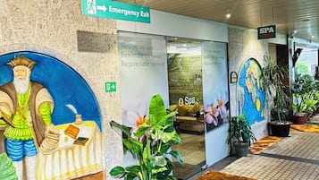A corridor with an emergency exit sign, a spa sign, and a mural with a figure holding a book.