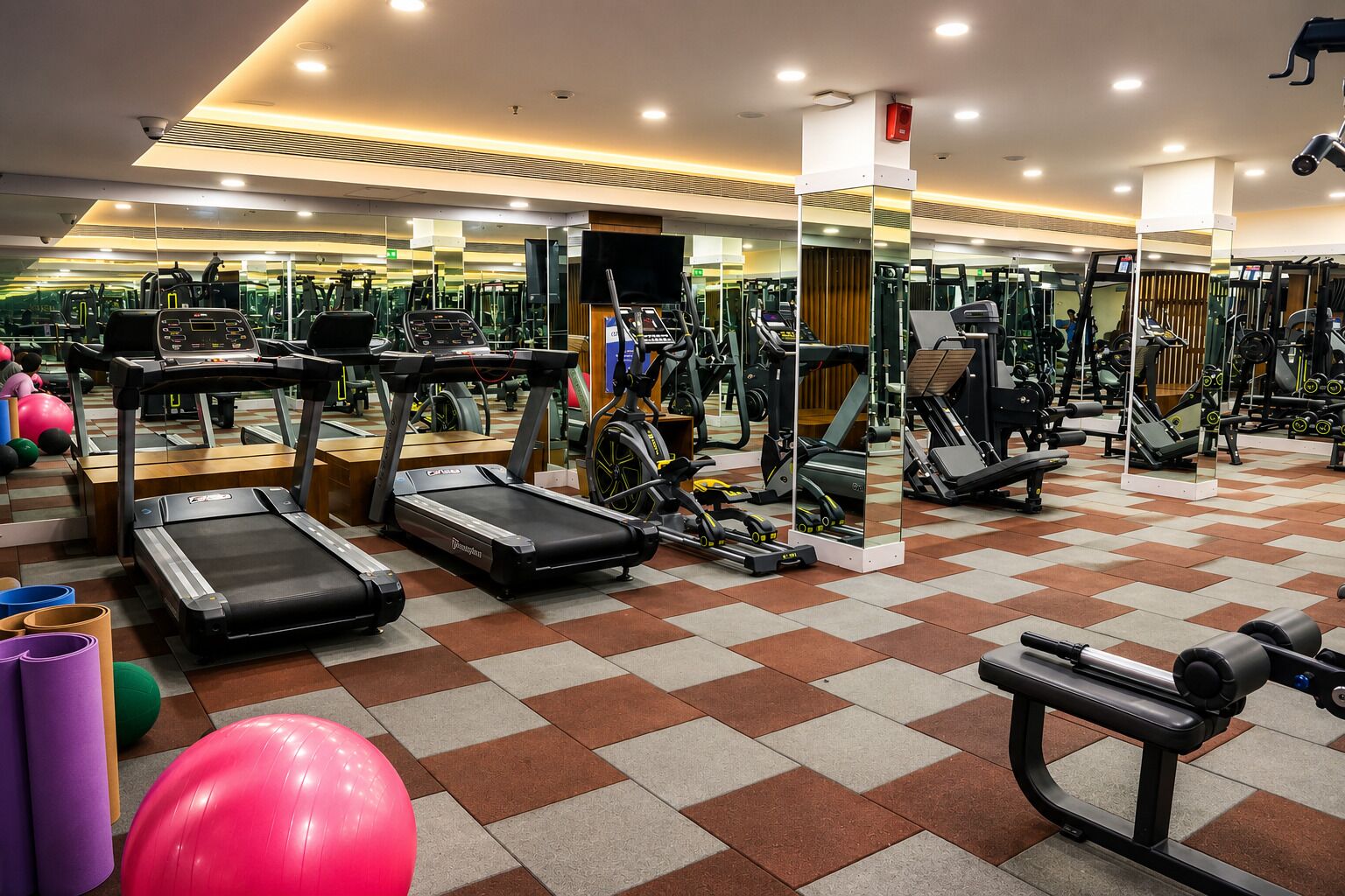 Academia com esteiras, bicicletas ergométricas e bolas de exercício.