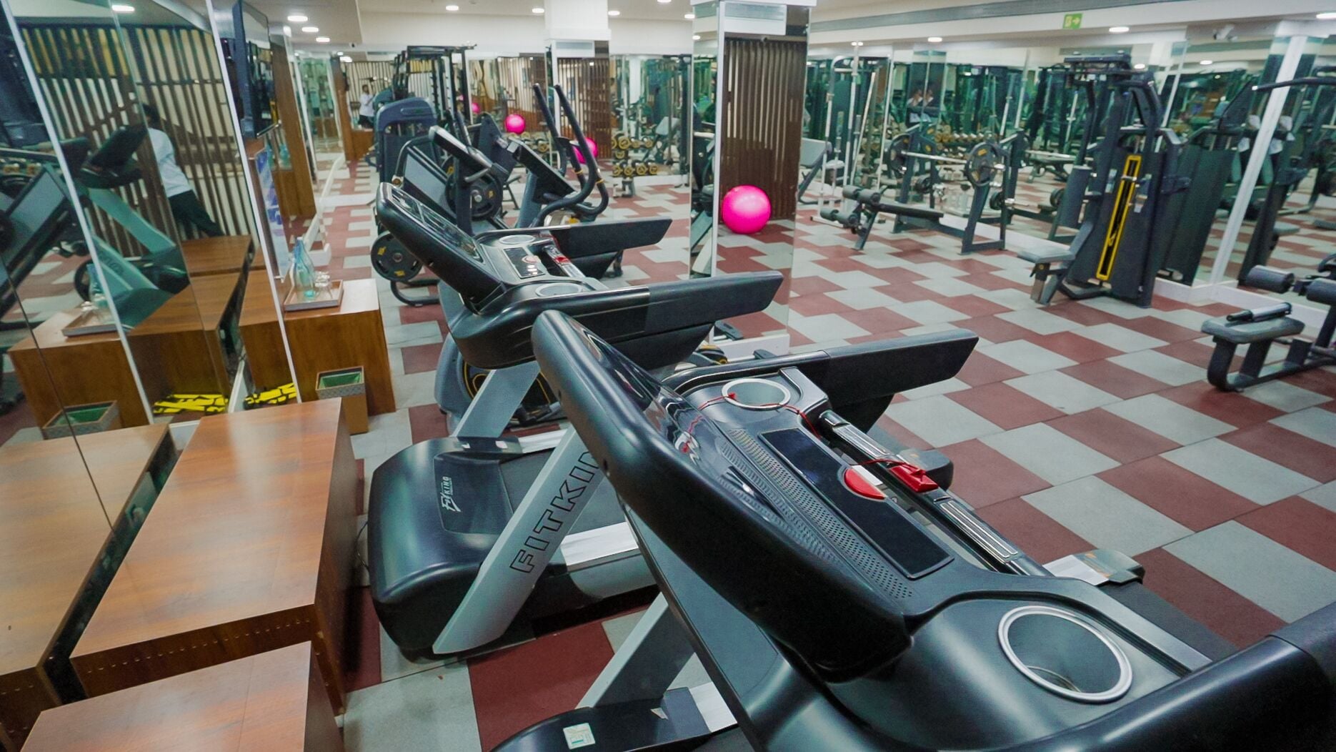 Un gimnasio con cintas de correr, máquinas de pesas y espejos.