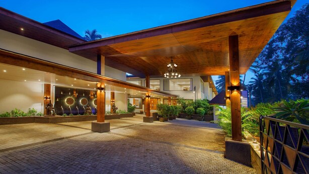 A modern hotel entrance with a covered walkway, potted plants, and a well-lit facade. - Sobit Sarovar Portico Goa (Canacona)