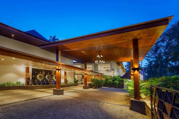 A modern hotel entrance with a covered walkway, potted plants, and a well-lit facade. - Sobit Sarovar Portico Goa (Canacona)