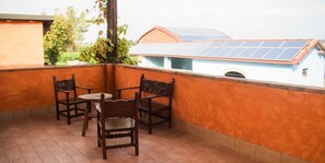 Een balkon met een tafel en stoelen, uitzicht op een gebouw met zonnepanelen en een boom.