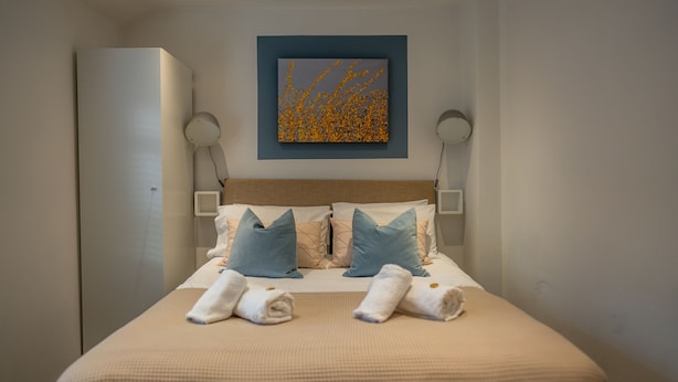 Una cama bien hecha con dos almohadas, una obra de arte en la pared y una lámpara de noche.