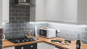 Una cocina moderna con baldosas grises, microondas integrado, estufa a gas y encimera de madera.