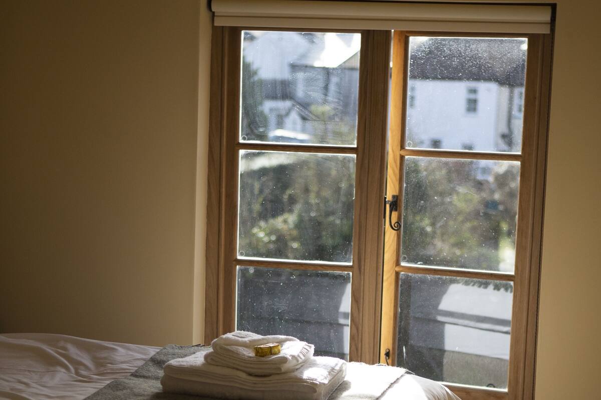 Une chambre d’hôtel avec un lit, une fenêtre donnant sur des immeubles et une pile de serviettes sur le lit.