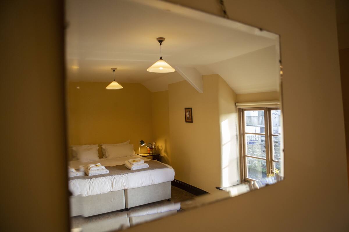 Une chambre à coucher avec un lit, deux lampes suspendues, une table de chevet et une fenêtre donnant sur un beau paysage.