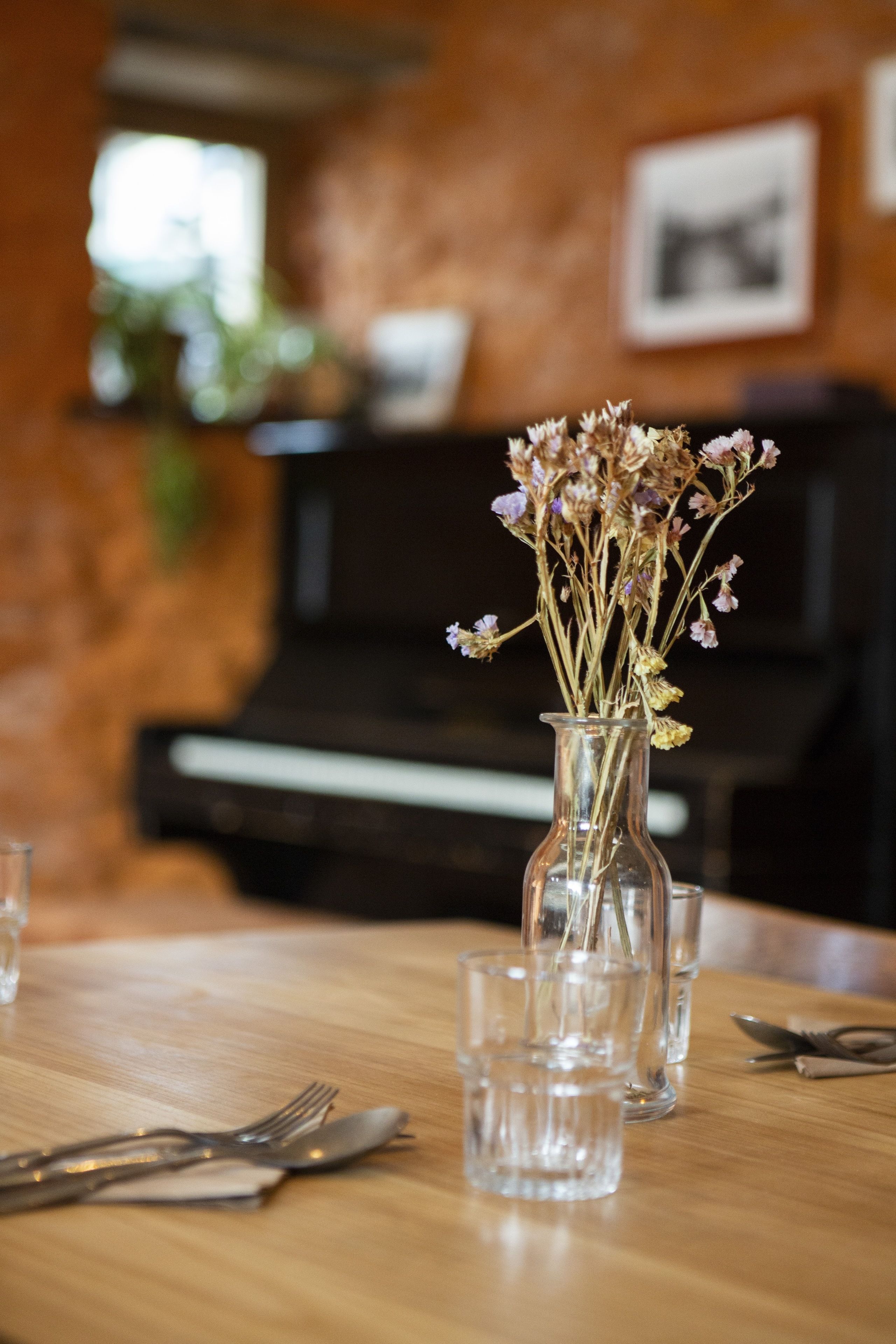 Una mesa de comedor con un florero de flores secas, cubiertos y vasos.