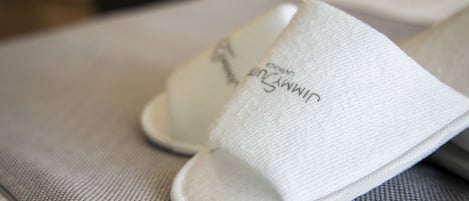 A pair of white slippers with embroidered text on the side, placed on a textured surface.
