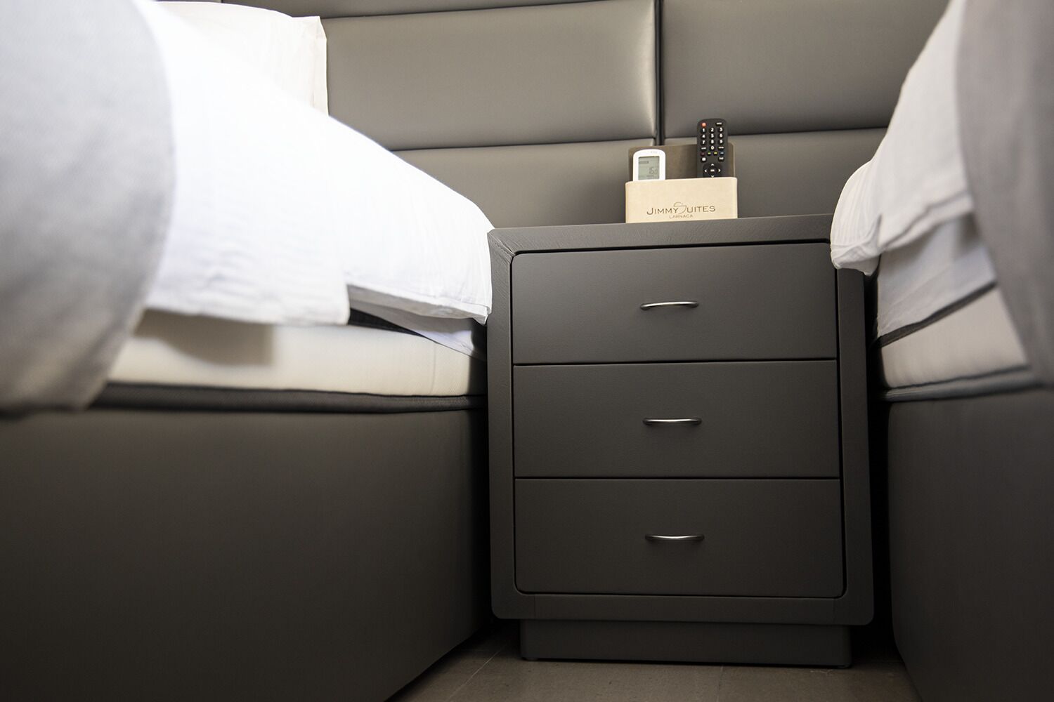 A modern bedroom with a gray headboard, a bedside table with a charging station, and a neatly made bed.