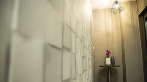 Un corridoio con carta da parati a motivi, un tavolino con un vaso e fiori, e una lampada a sospensione geometrica.