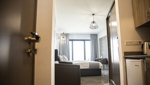 Una moderna camera d'albergo con un letto, una poltrona, un'area pranzo e un angolo cottura.