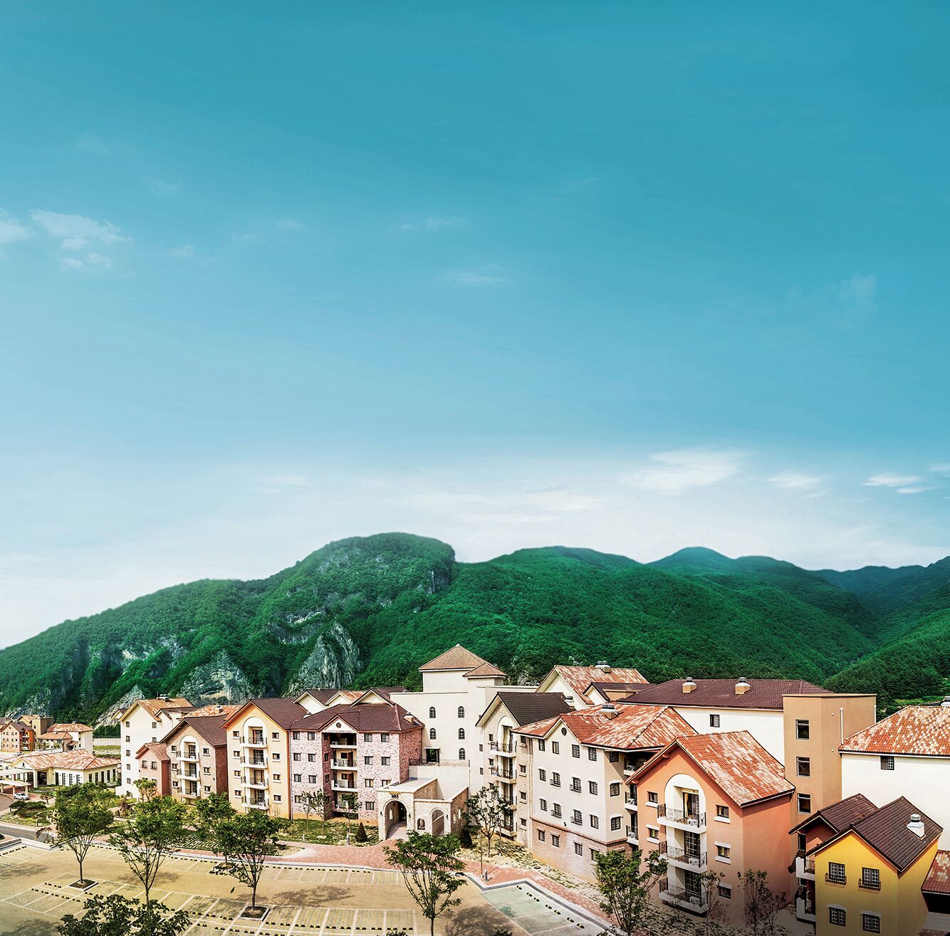 A residential area with multi-story buildings, a parking lot, and a mountainous backdrop.