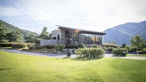 Een modern huis met een glazen gevel, omringd door een verzorgd gazon en met bergen op de achtergrond.