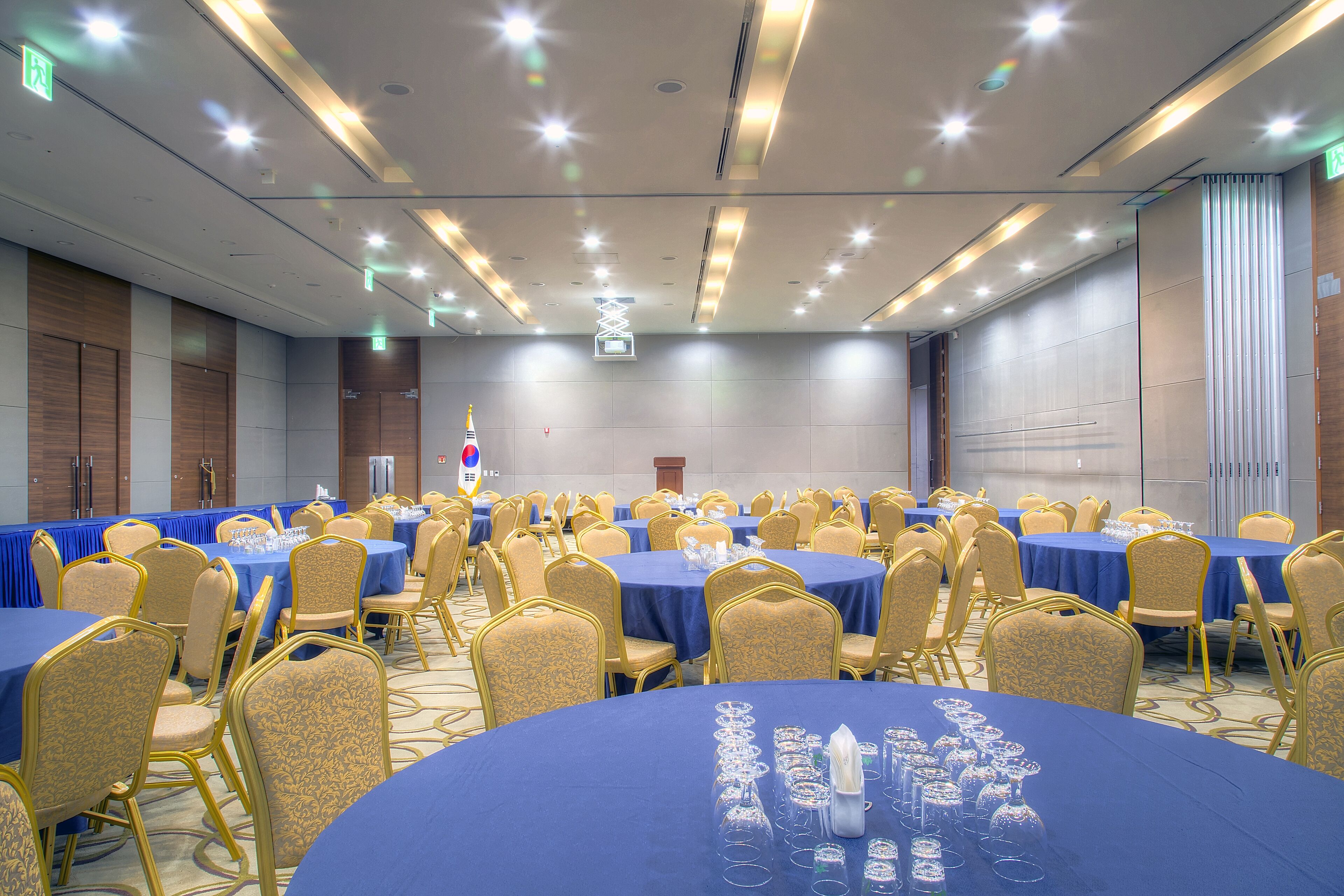 Un salón de conferencias con varias mesas y sillas, equipado con cristalería y un atril.