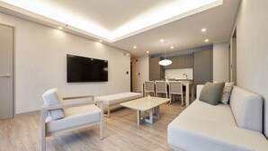 Een moderne woonkamer met een bank, een lange hocker, een tafel en een aan de muur bevestigde televisie.