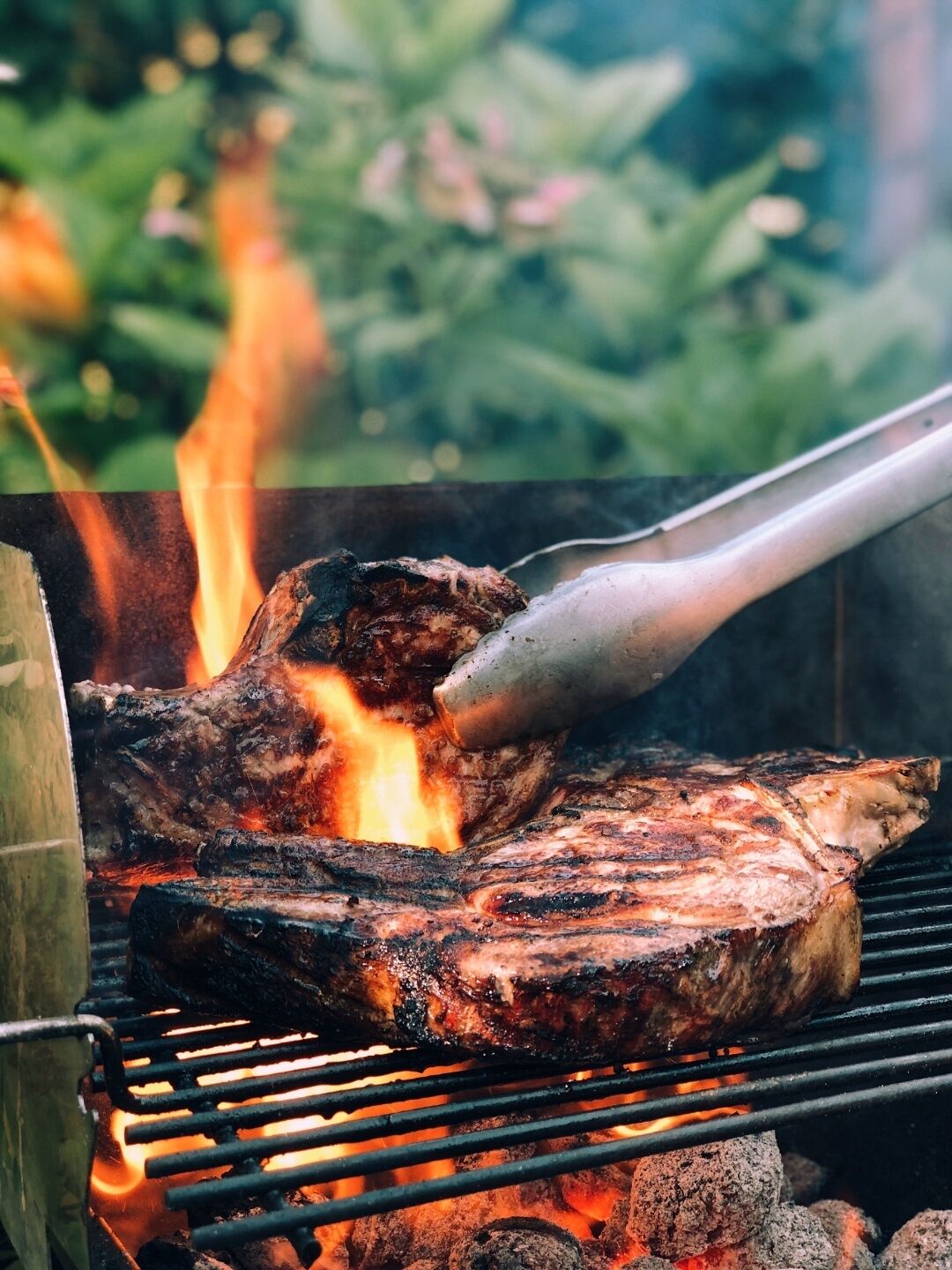 Ein Steak wird auf einem Holzkohlegrill mit sichtbaren Flammen gegrillt.