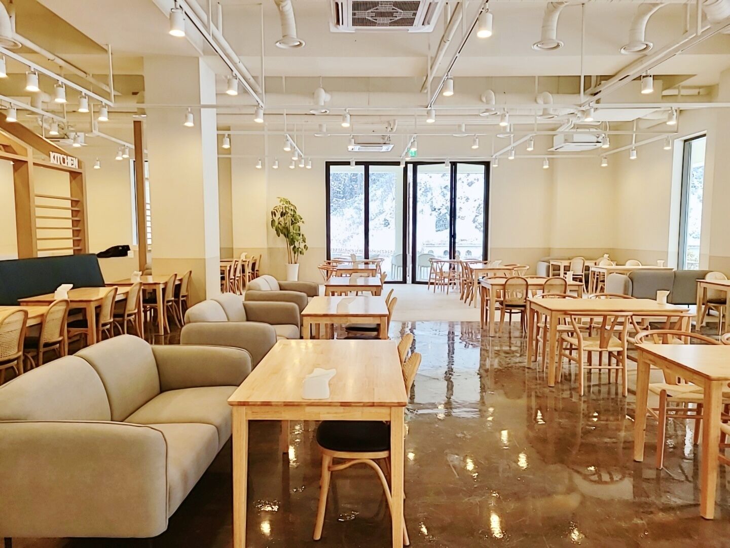 A spacious cafe with multiple seating areas, including tables and sofas, and a visible kitchen area.