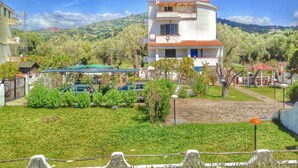 Un edificio a due piani con facciata bianca e tetto in tegole rosse, immerso nel verde e con uno sfondo collinare.