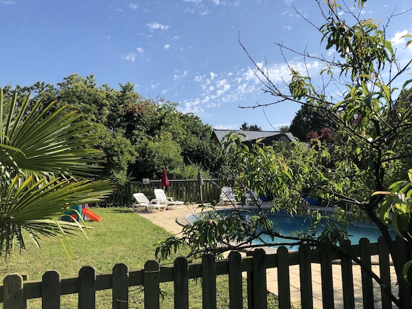 A backyard with a pool, a wooden fence, and a house in the background. - Chambres d'hotes Bastia et Bonifacio (Retiers)