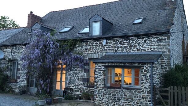 Una casa de piedra con techo inclinado, varias ventanas y un pequeño porche.