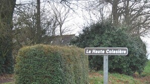 Una señal de calle que dice 'La Haute Colasière' en un entorno rural con follaje denso y árboles al fondo.