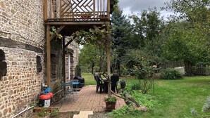 Un edificio de piedra con un balcón de madera, mobiliario exterior y un jardín.