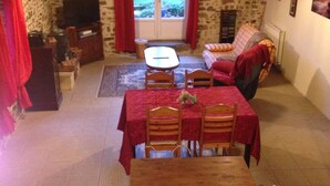 Una sala de estar acogedora con una pared de piedra, una mesa de comedor con sillas, un sofá y un televisor.